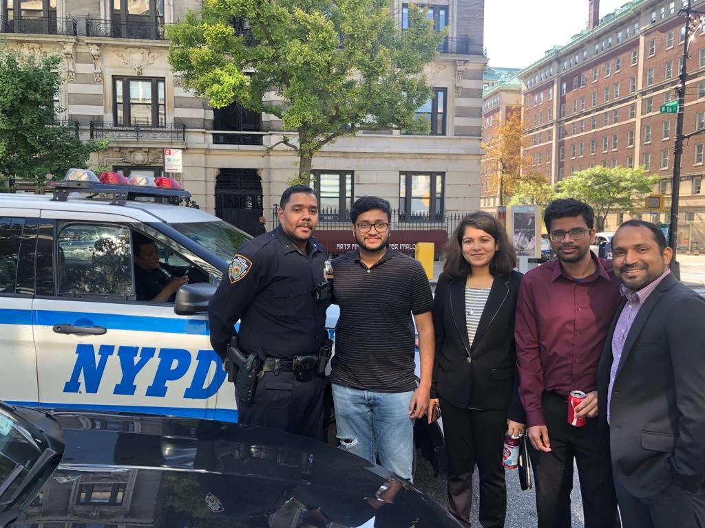 Zenext team members speaking with a police officer beside a patrol vehicle in New York City.